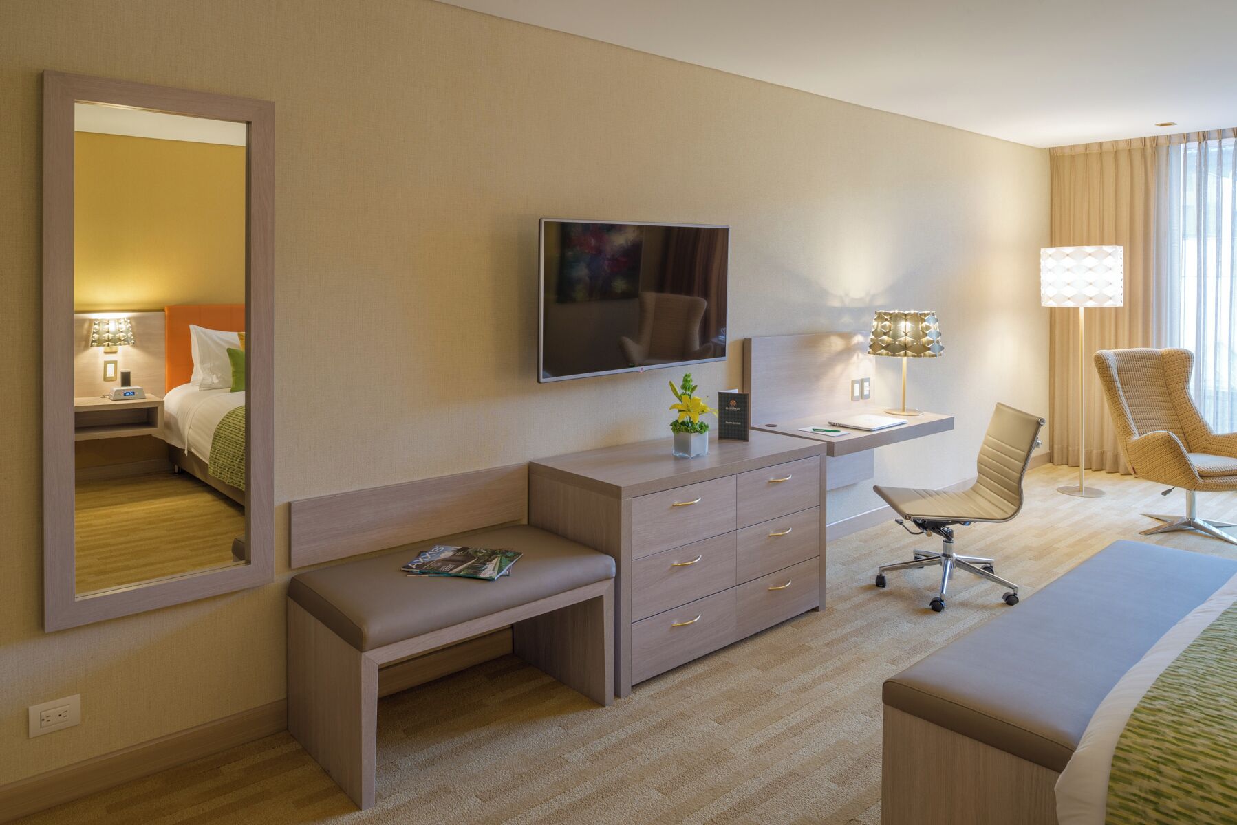Camera d'albergo con un letto, una scrivania con sedia, uno specchio grande, una televisione e una lampada.