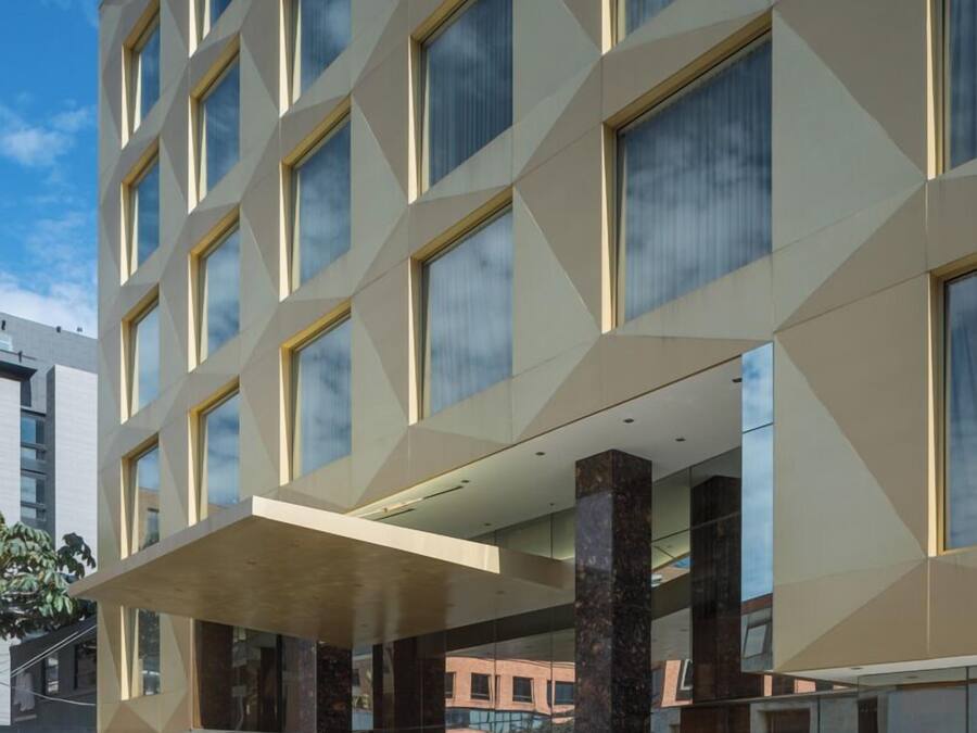 Un hotel moderno con facciata geometrica, ampie finestre e un'area d'ingresso coperta con piante in vaso.