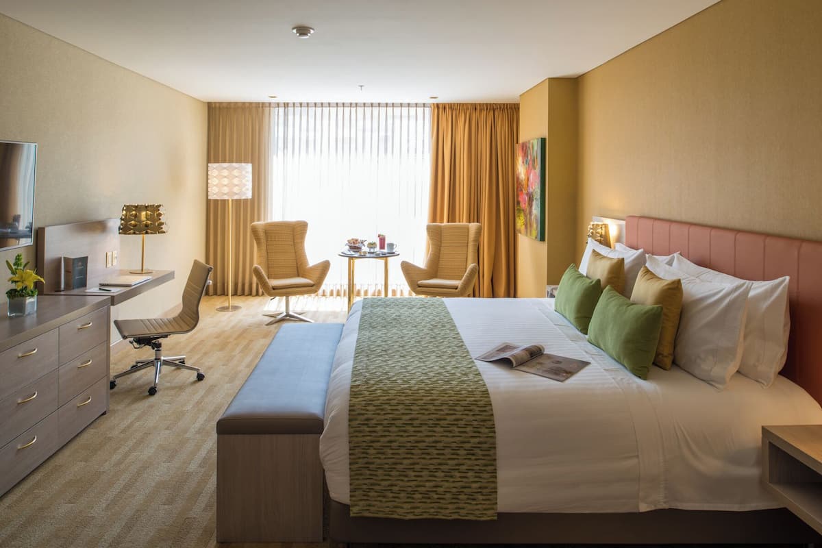A hotel room with a large bed, two armchairs, a desk, and a television.