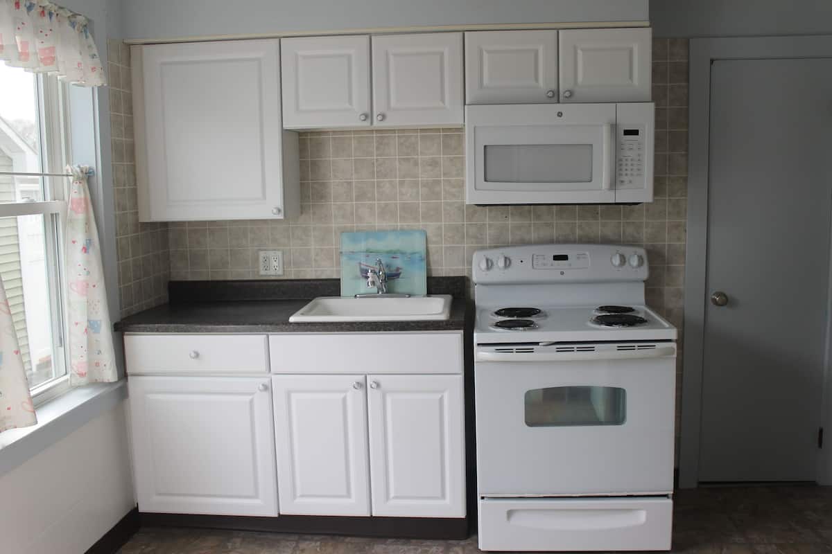 A kitchen with white cabinets, a microwave, a stove, and a sink.