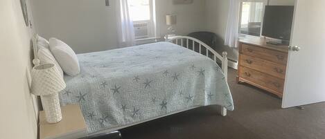 A bedroom with a bed, a dresser, a chair, and a television.