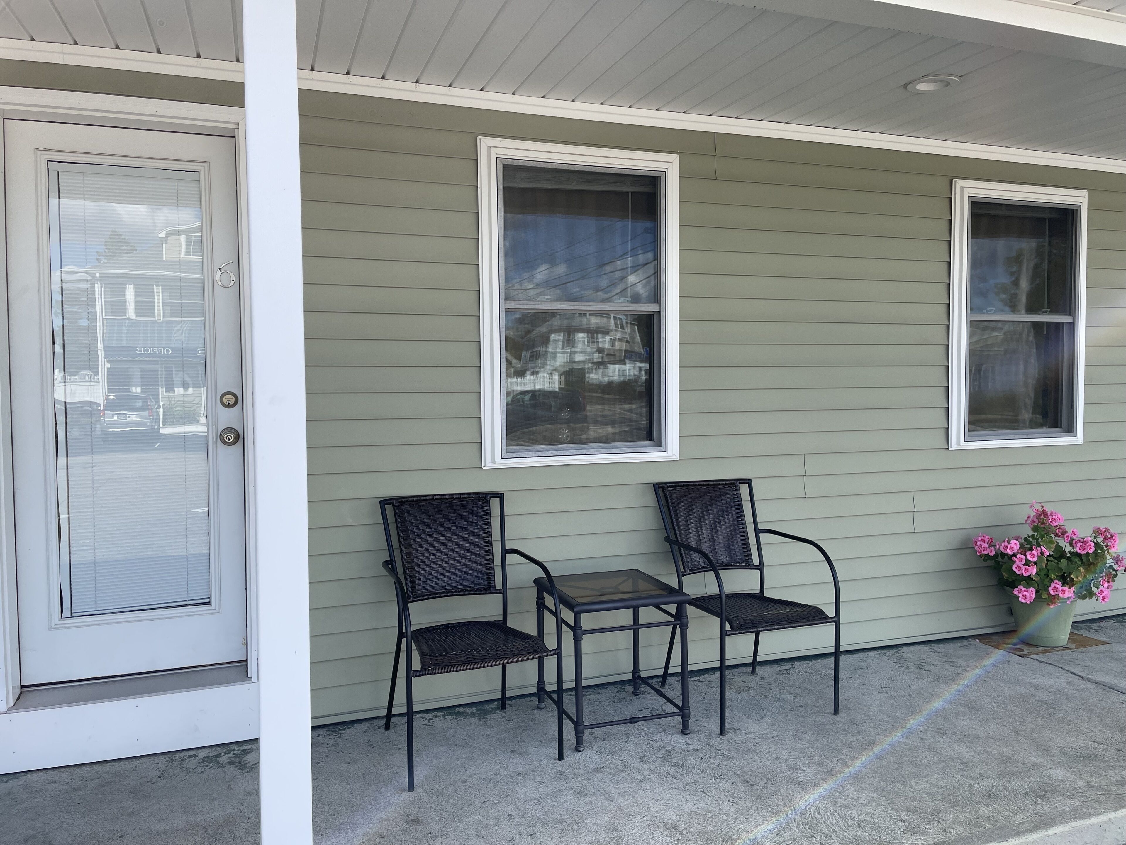 A porch with two chairs and a table, a door, and a window with a flower pot.