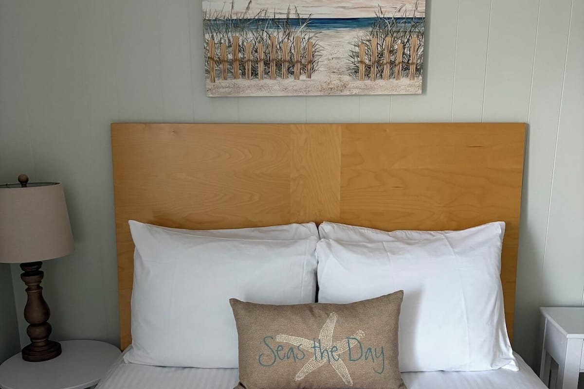 A neatly made bed with striped bedding, a wooden headboard, and a pillow with "Seas the Day" text.