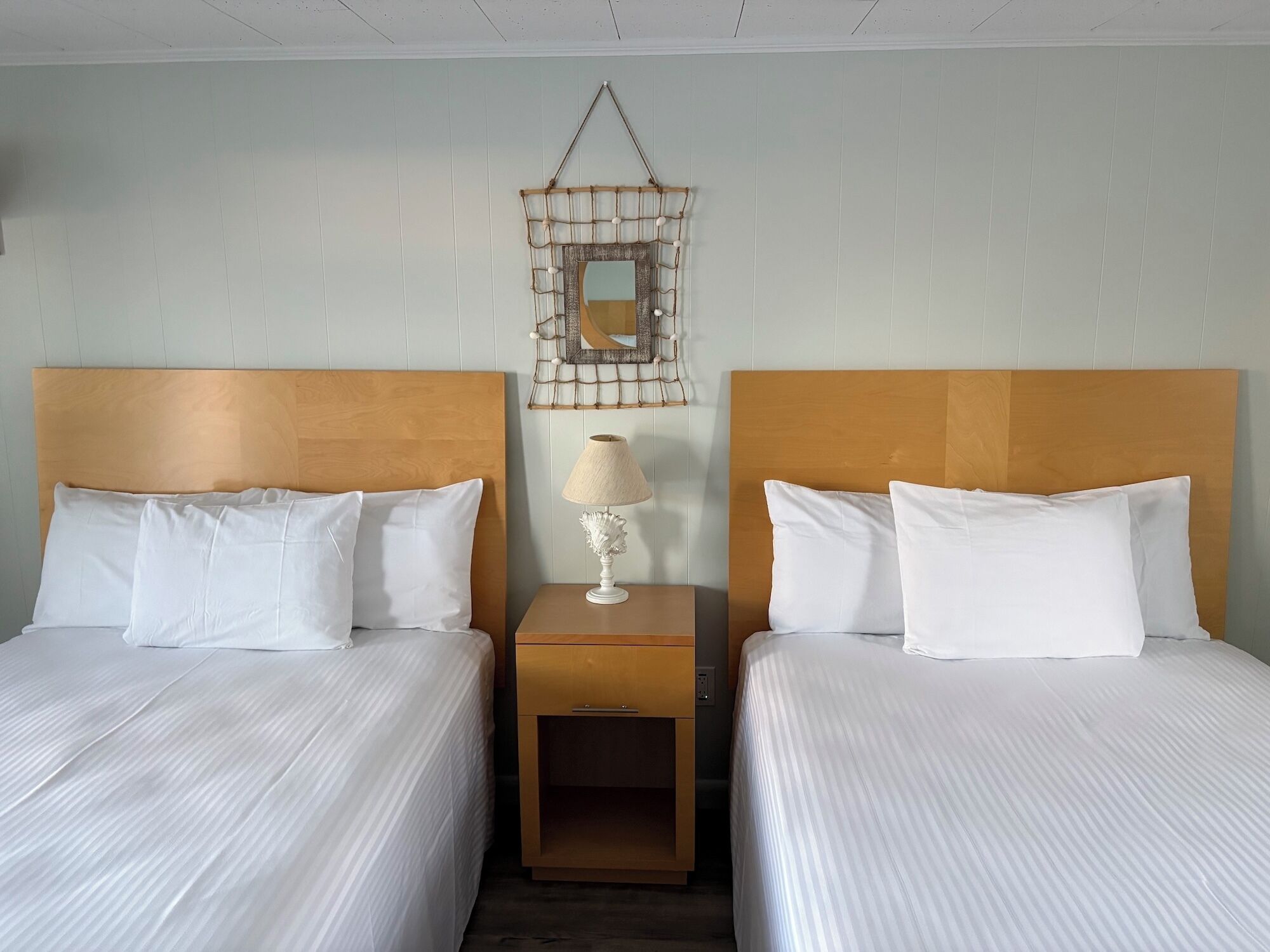 Een hotelkamer met twee bedden, een nachtkastje met een lamp en een spiegel aan de muur.