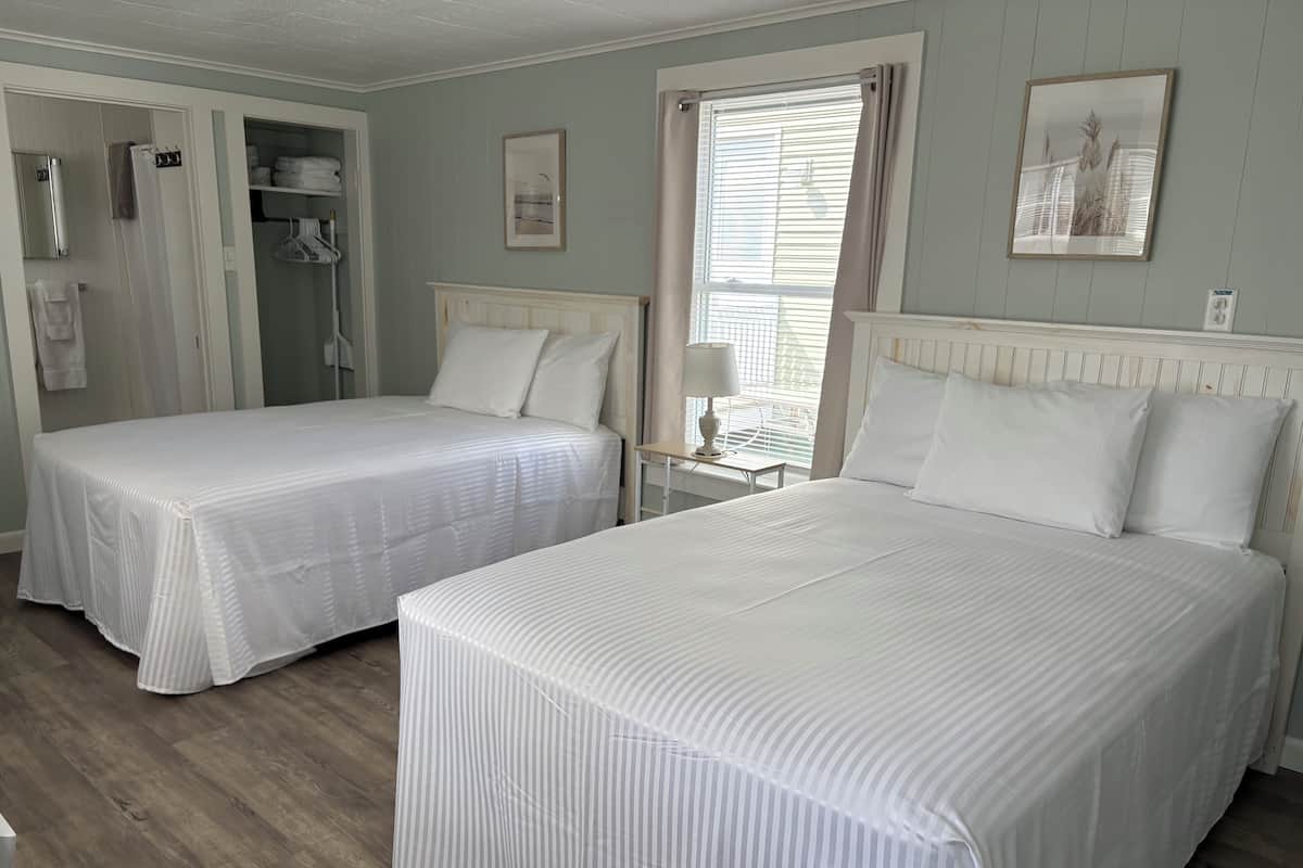 A hotel room with two beds, a walk-in closet, and a window with blinds.