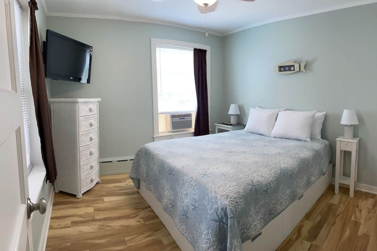 A bedroom with a bed, dresser, TV, window, and two bedside tables.