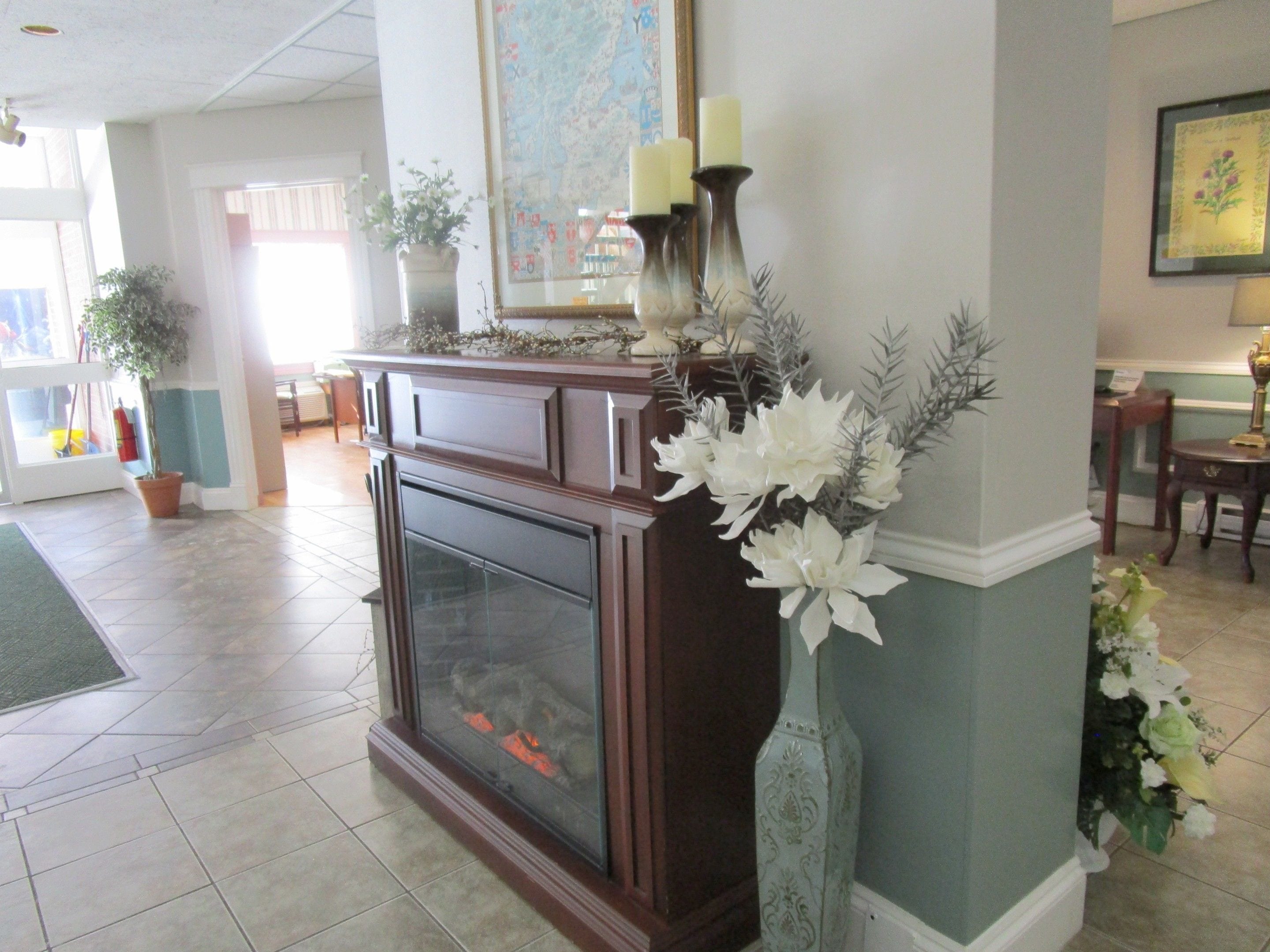 A fireplace with decorative flowers and candles, a potted plant, and a framed map on the wall.