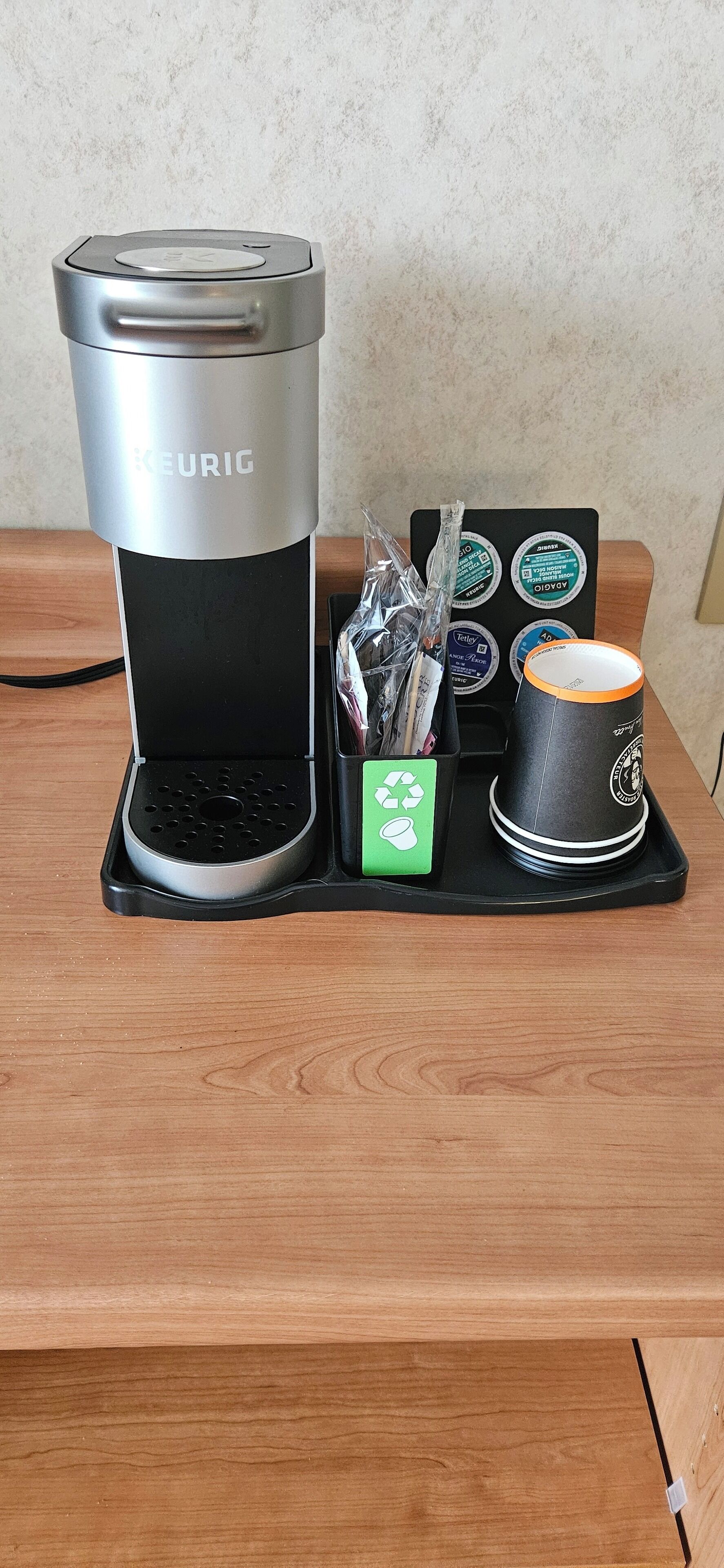 Una cafetera Keurig con un portacapsulas de café y una taza sobre una mesa de madera.