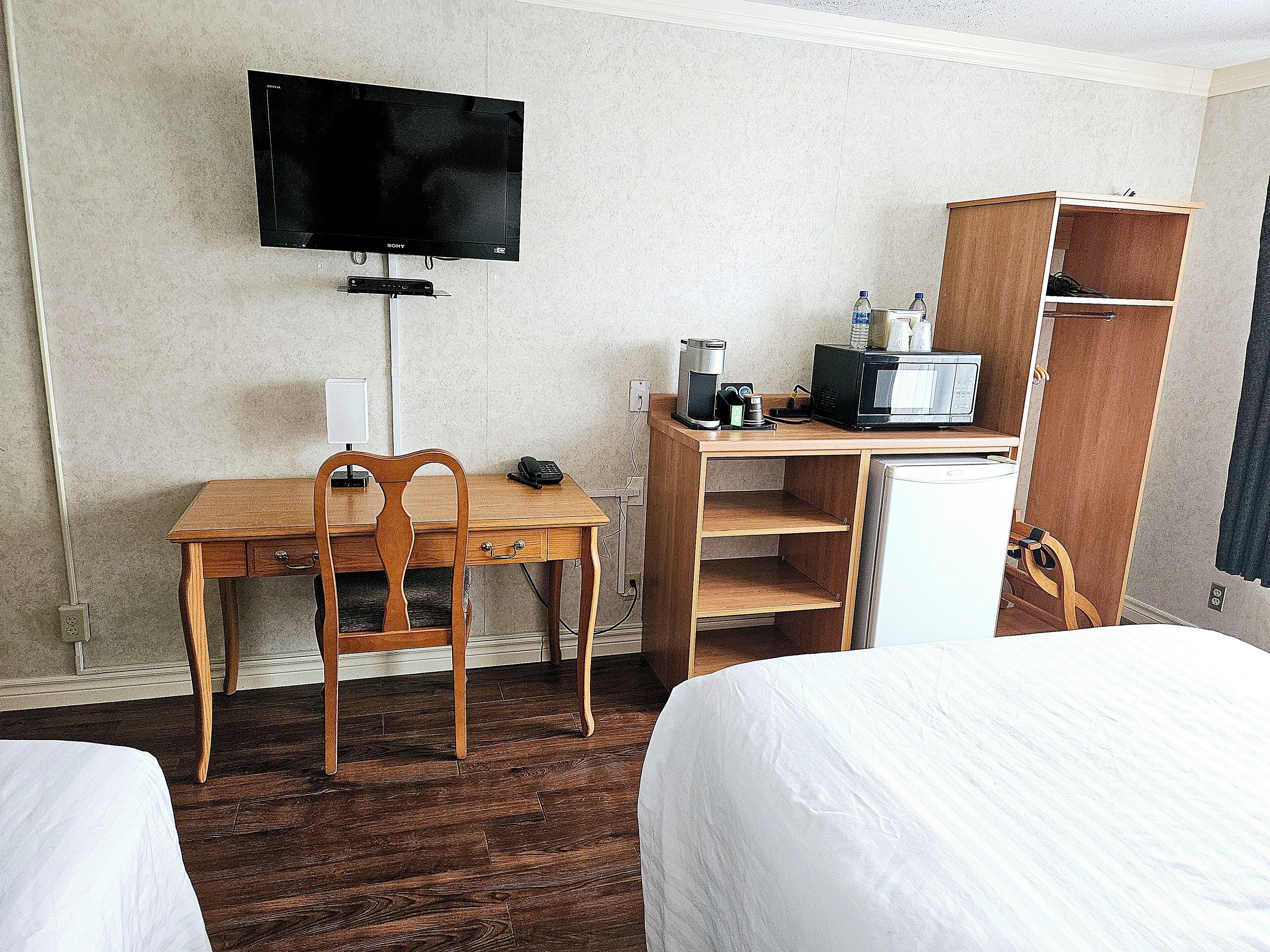 A hotel room with a wooden desk, a television, a coffee maker, and a wardrobe.