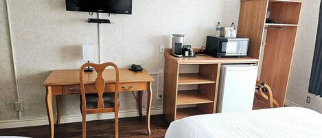 Une chambre d’hôtel équipée d’un bureau en bois, d’une télévision, d’une machine à café et d’une armoire.