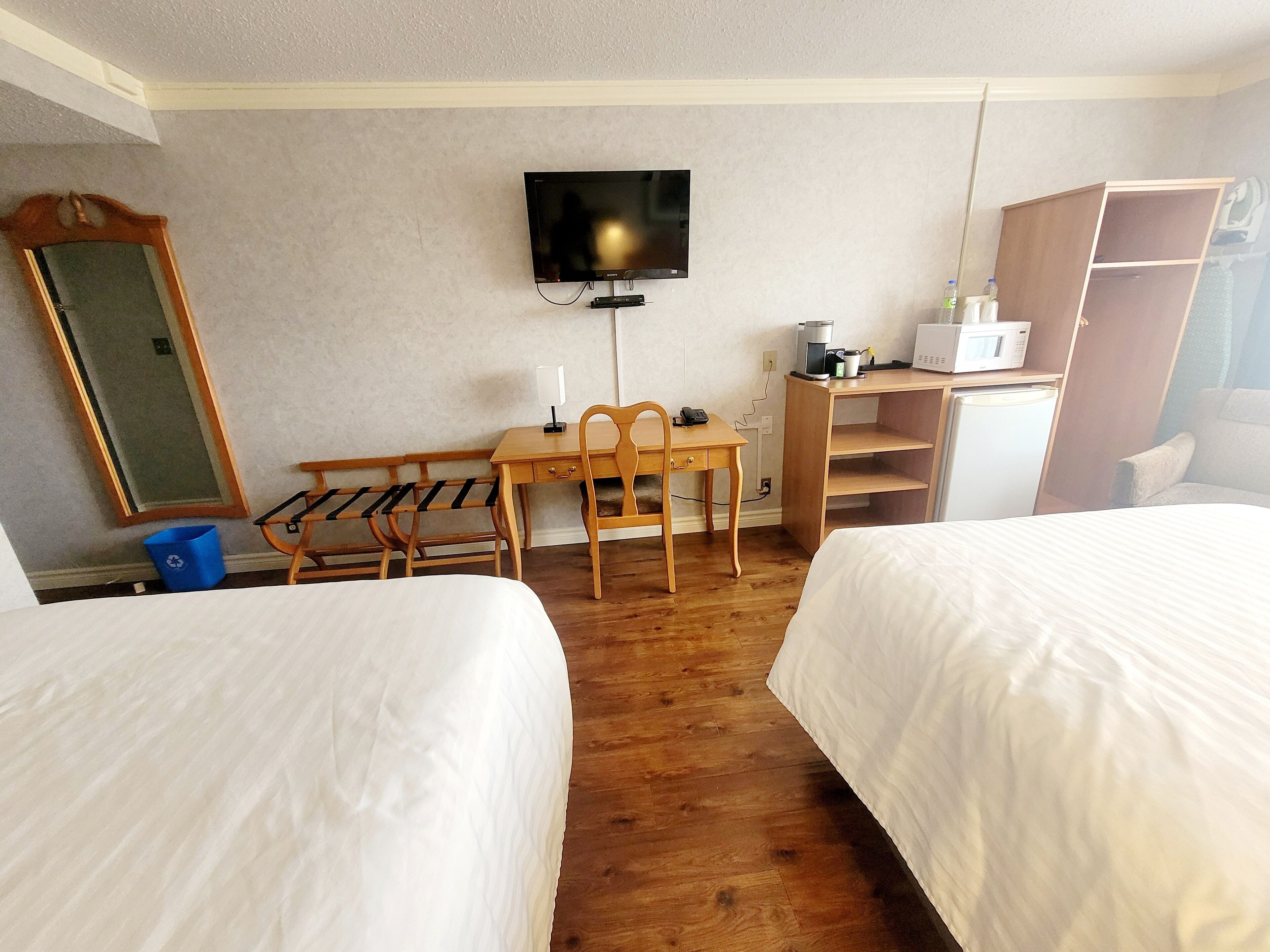 A hotel room with two beds, a desk with a chair, a television, a microwave, and a small refrigerator.