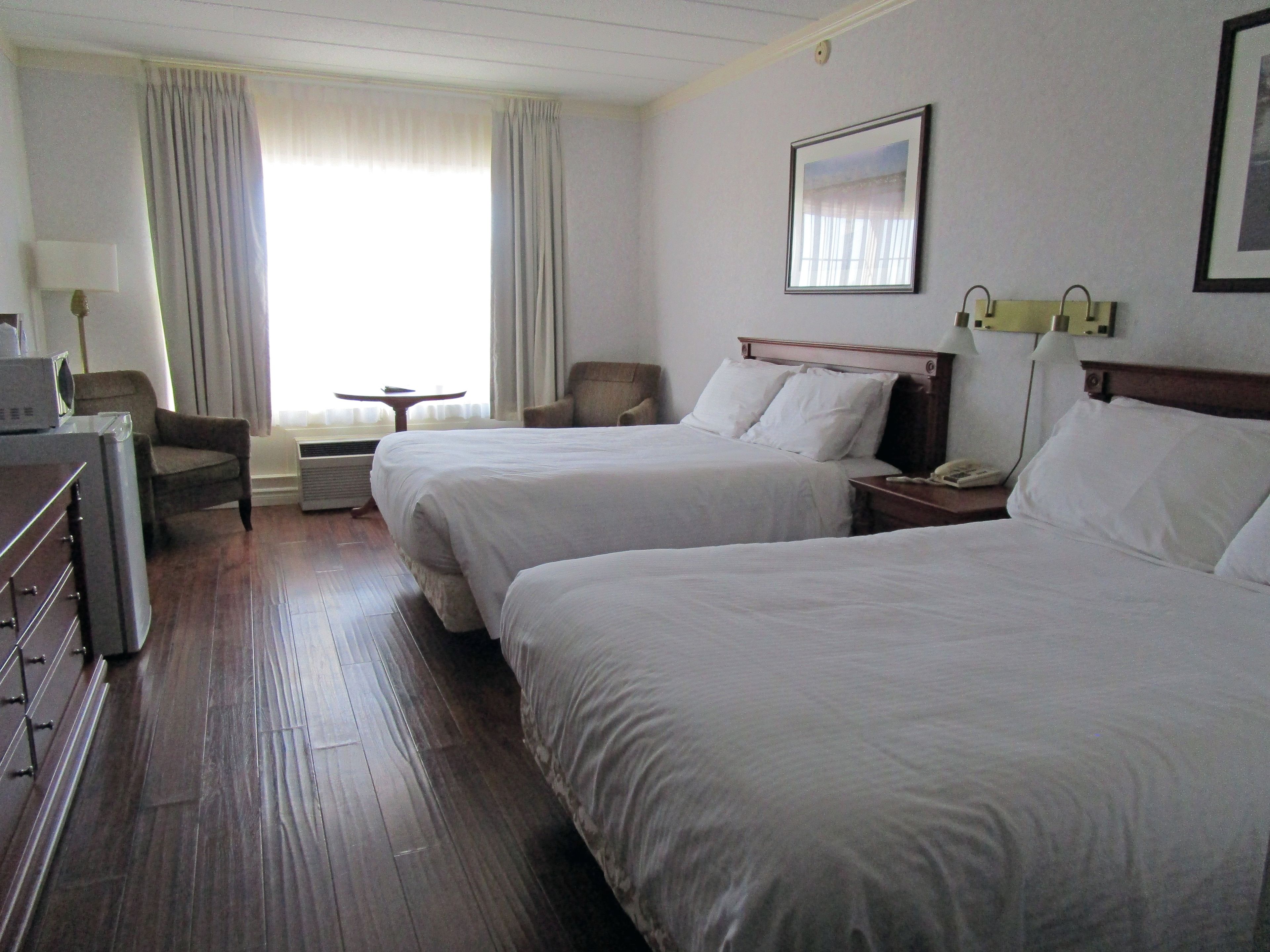 Une chambre d’hôtel avec deux lits, un bureau, une chaise, une petite table et une fenêtre avec des rideaux.