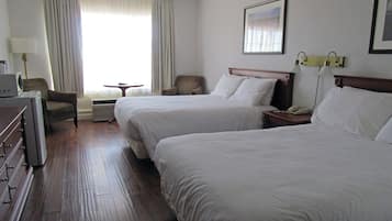 Une chambre d’hôtel avec deux lits, un bureau, une chaise, une petite table et une fenêtre avec des rideaux.
