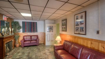 A living room with a fireplace, a red leather sofa, a wooden bench, and a wall with framed pictures.