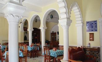 A dining area with tables and chairs, white columns, and a patterned floor.