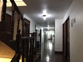 A long, narrow hallway with wooden railings on one side and a plain wall on the other.