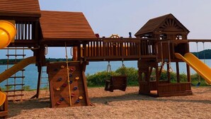 Un parque infantil de madera con toboganes y estructuras para escalar cerca de un lago.