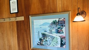 Una habitación con paneles de madera, un cuadro enmarcado que muestra una escena costera, una lámpara y un sofá.
