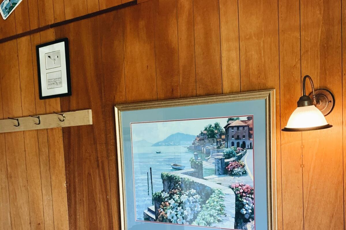 A wooden-paneled room with a framed painting of a coastal scene, a light fixture, and a sofa.
