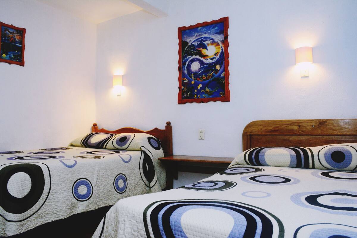 A bedroom with two beds, each with a circular-patterned bedspread, a wooden headboard, and a wall-mounted light fixture.