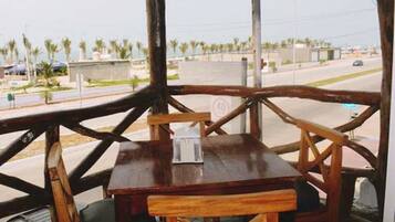 Relax in a serene outdoor seating area with a table and chairs, surrounded by a wooden structure and a view of the surrounding street with palm trees and buildings.