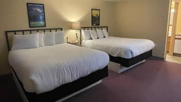 A hotel room with two beds, a nightstand with a lamp, and a door leading to a bathroom.