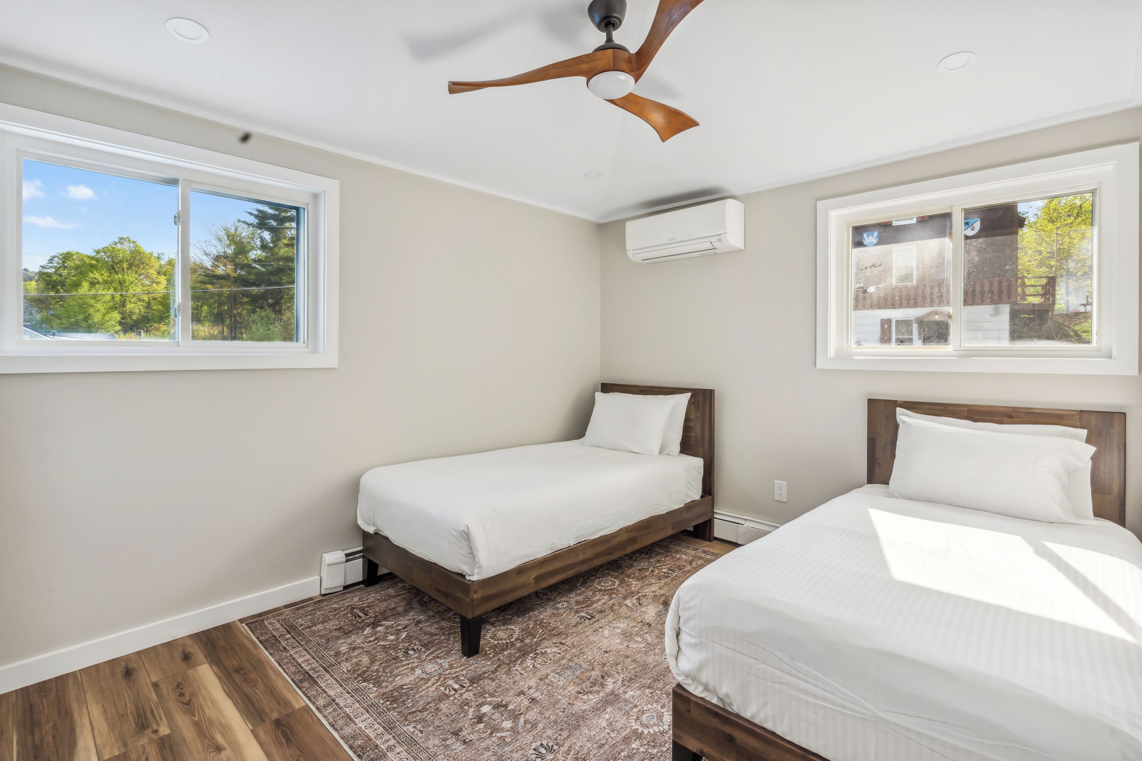 Une chambre avec deux lits, un ventilateur de plafond et de grandes fenêtres donnant sur la verdure.