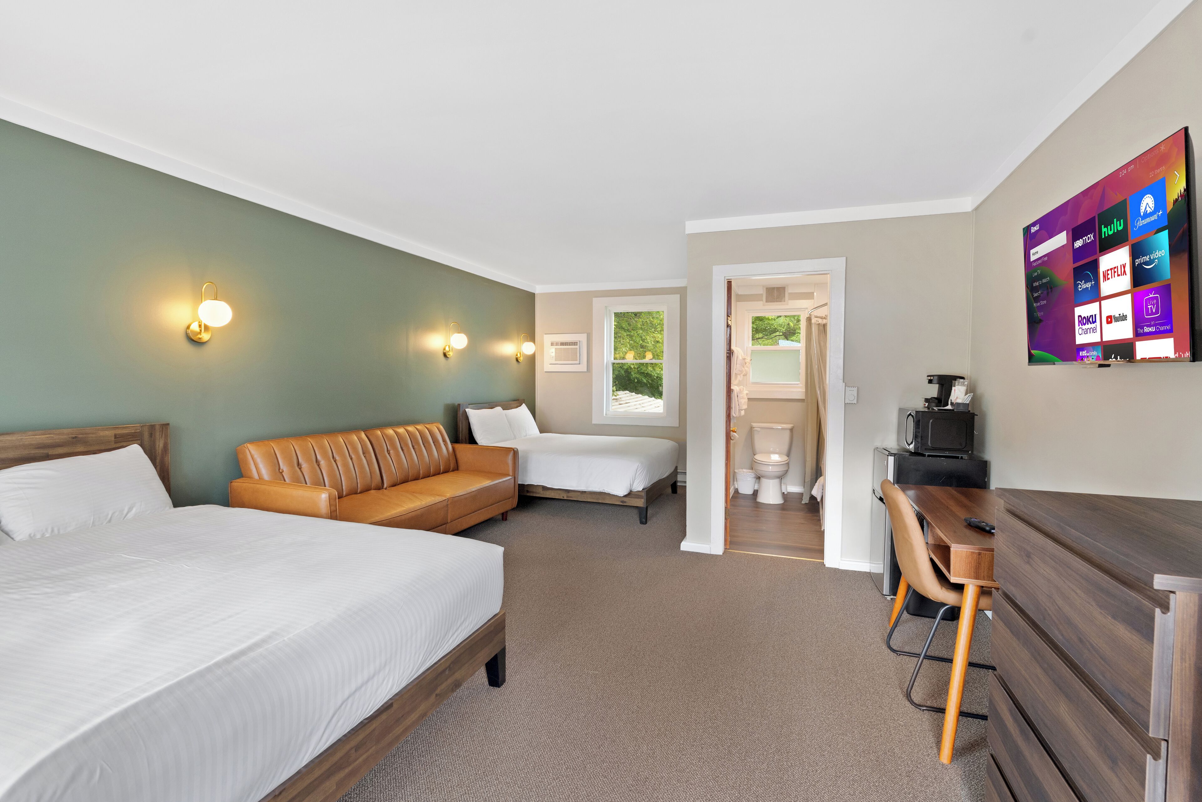 A hotel room with a bed, a sofa, a desk, and a TV displaying streaming services.