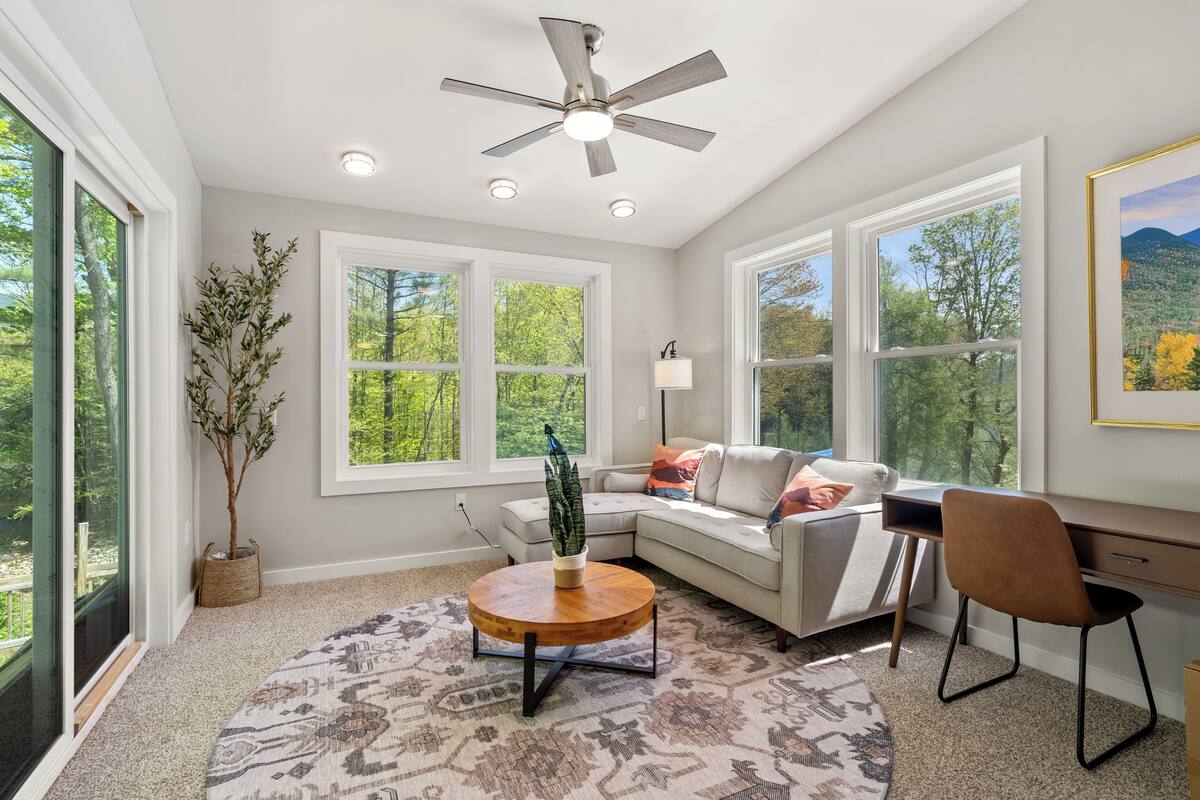 A spacious living room with a large window, a ceiling fan, a round coffee table, a sofa, and a desk.