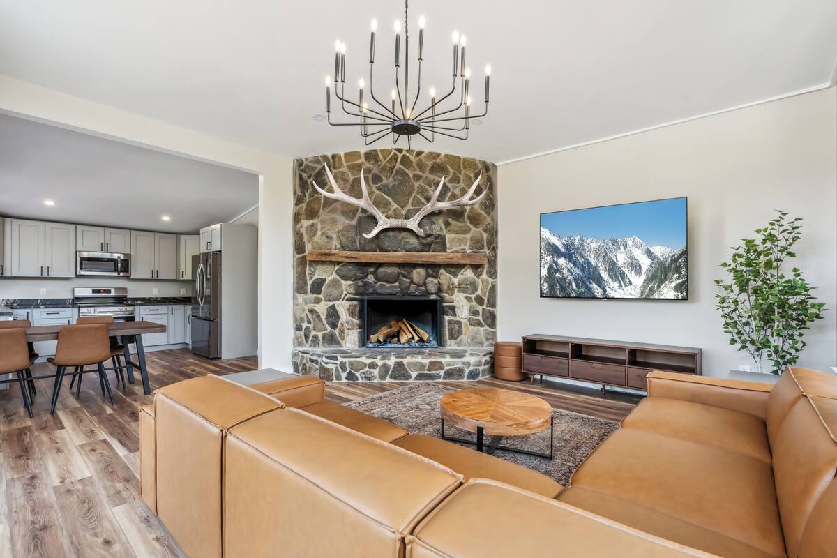 A modern living room with a stone fireplace, leather sofas, and a dining area with a kitchen in the background.