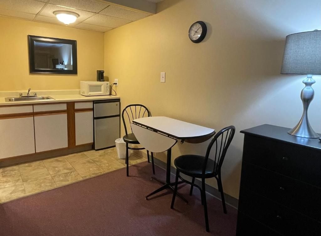 Una kitchenette compacta con microondas, pileta y heladera pequeña. Hay una mesa de comedor con dos sillas y un reloj en la pared.