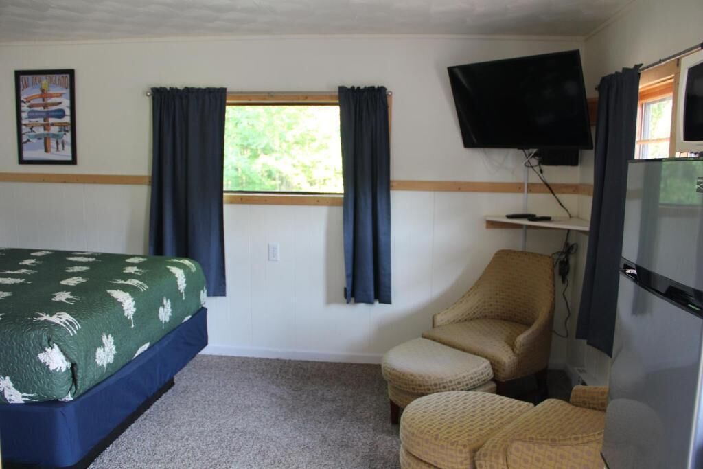 Una habitación con una cama, una silla, un televisor y un ventanal con cortinas.