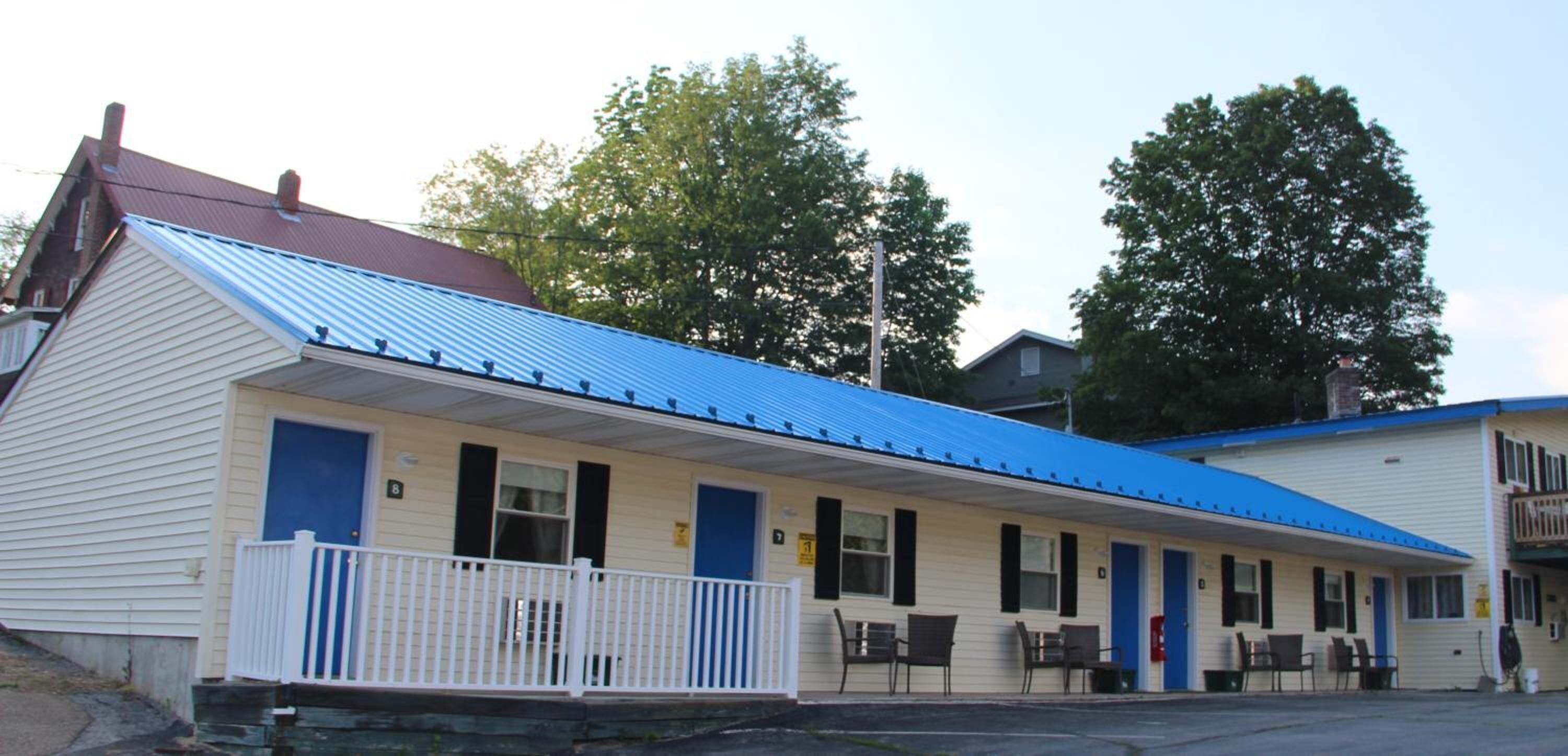 Un motel con techo azul y fachada blanca, que cuenta con un porche con sillas y una pequeña mesa.