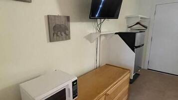 A room with a wooden dresser, a microwave, a flat-screen TV mounted on the wall, and a door in the background.