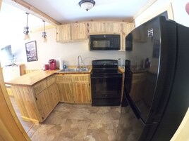 A compact kitchen with wooden cabinets, a black refrigerator, a microwave, a stove, and a sink.