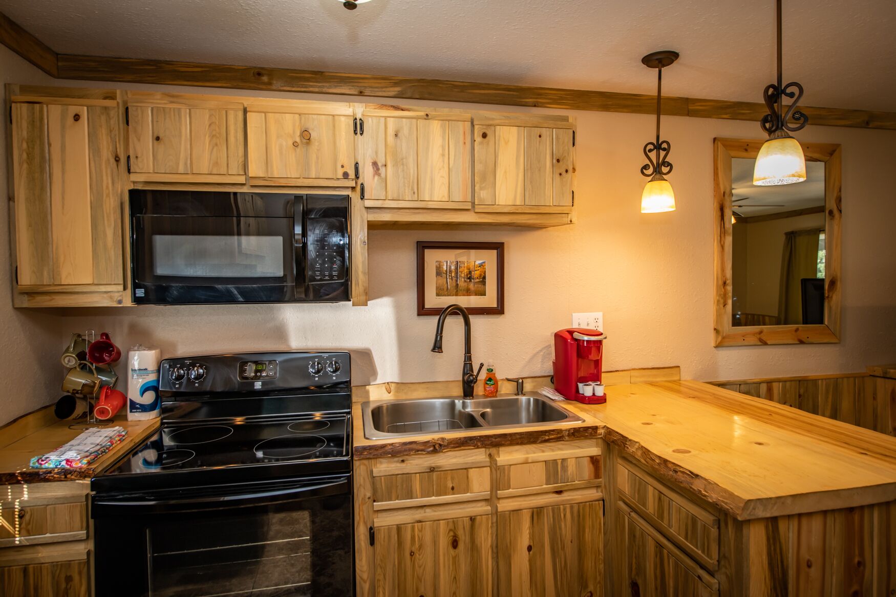 Une cuisine avec des meubles de rangement en bois, un évier en acier inoxydable, un four à micro-ondes, une cuisinière et une machine à café rouge.