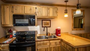 Une cuisine avec des meubles de rangement en bois, un évier en acier inoxydable, un four à micro-ondes, une cuisinière et une machine à café rouge.