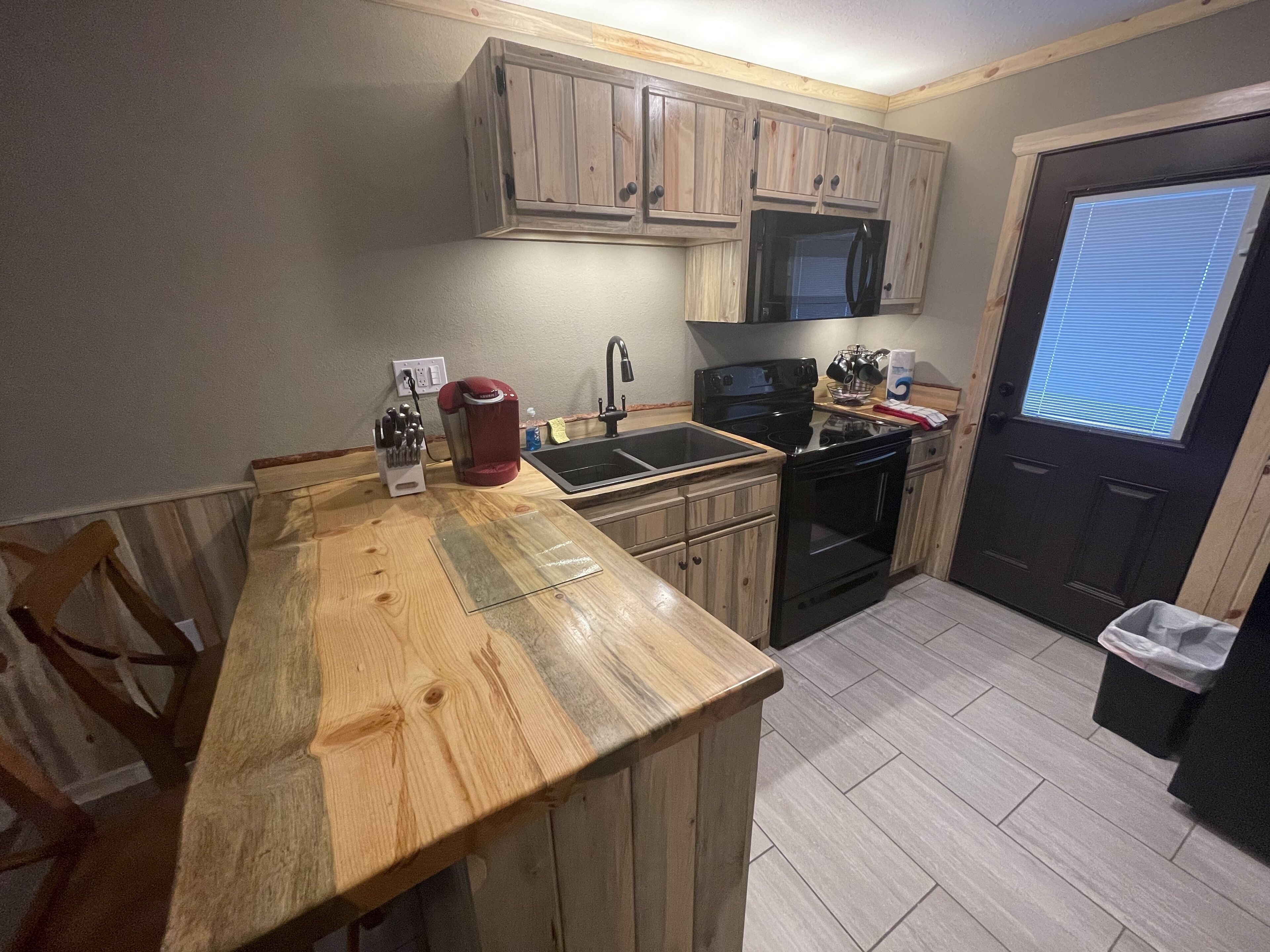 A kitchen with wooden cabinets, a black stove, a sink, and a coffee maker.