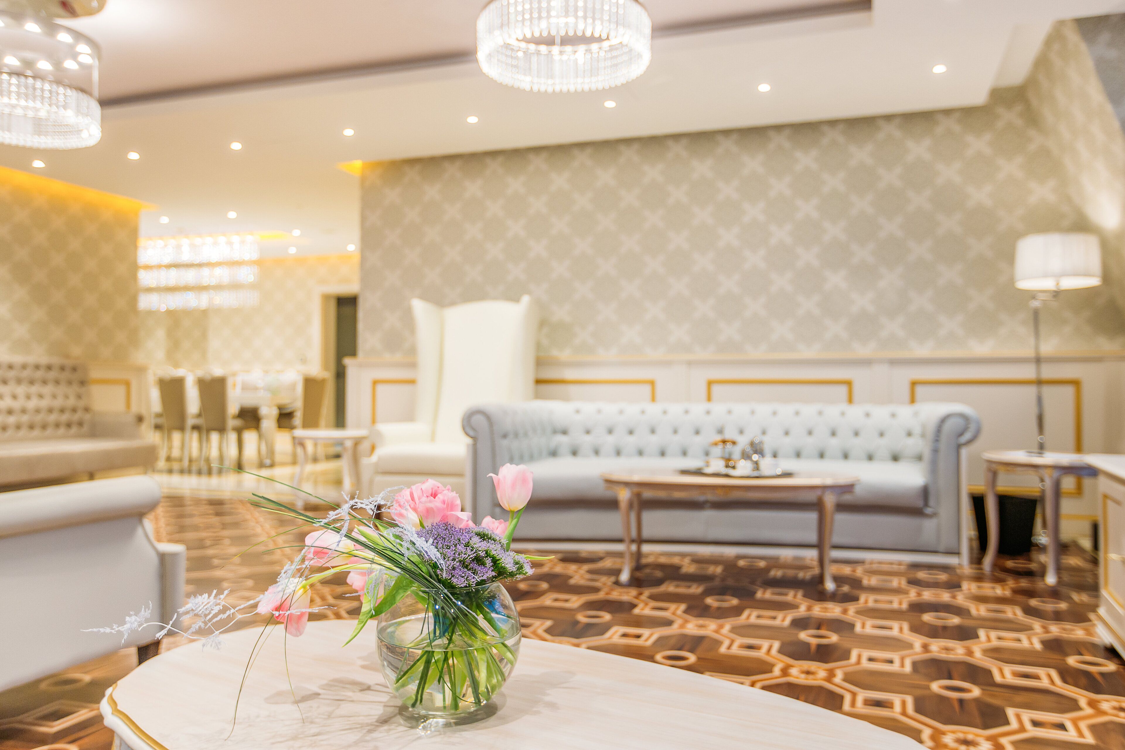 Un vestíbulo de hotel con alfombra estampada, un sofá, una mesa con un florero y una araña.