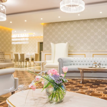 A hotel lobby with a patterned carpet, a sofa, a table with a vase of flowers, and a chandelier.