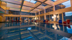 Een ruim binnenzwembad met glazen dak, meerdere lounges en moderne verlichting.