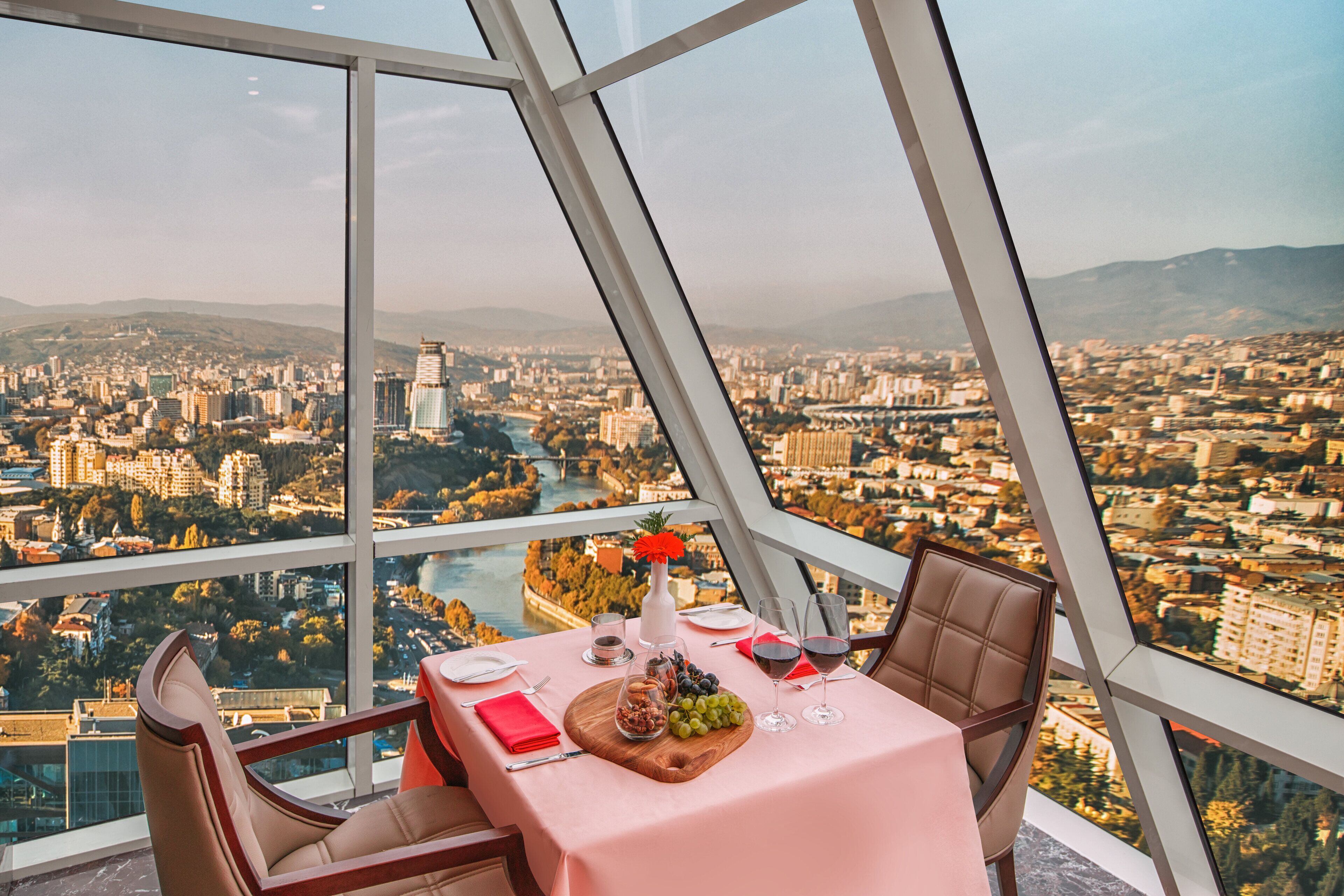 A table set for two with a city view, a vase with flowers, and a bottle of wine.