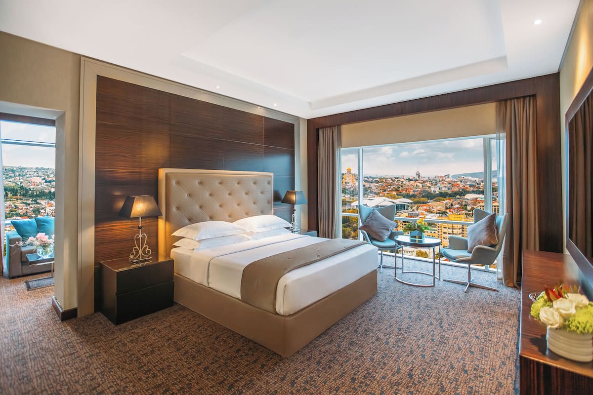 Ein Hotelzimmer mit einem großen Bett, einer Sitzecke mit Blick und einem Balkon mit Stadtansicht.
