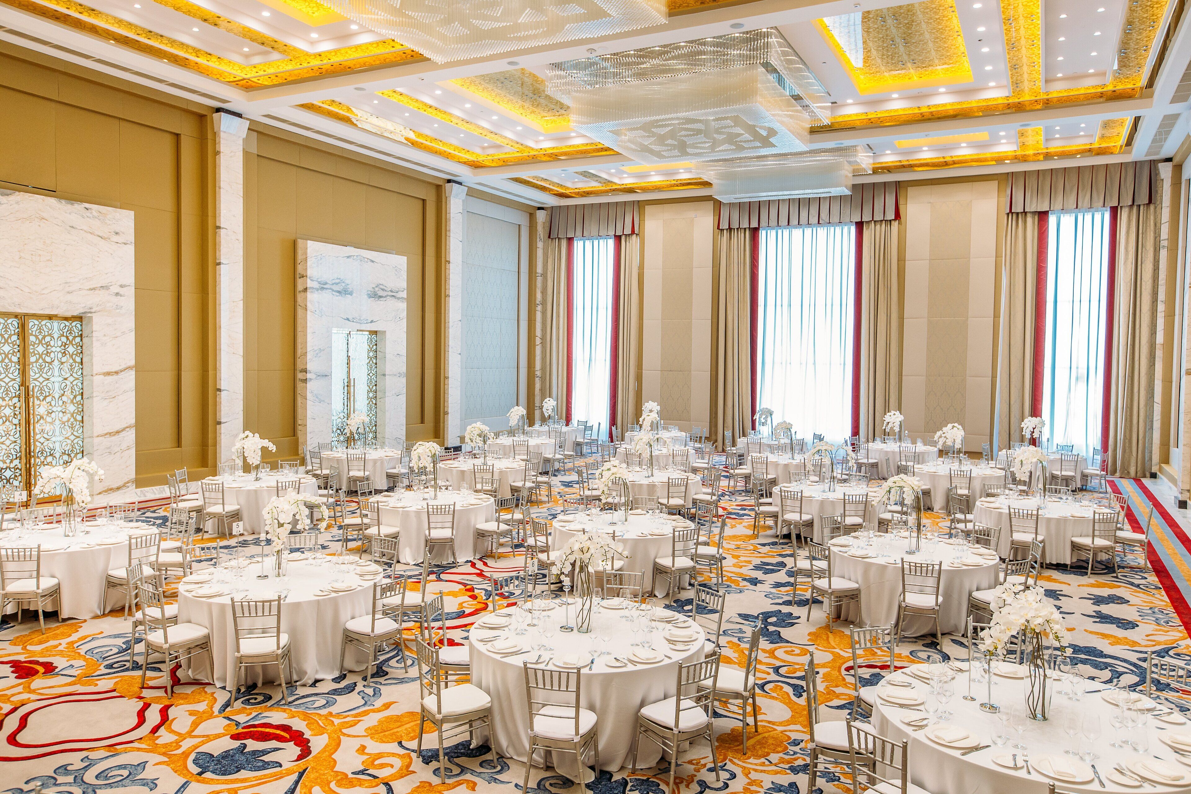 A large banquet hall with round tables, white tablecloths, and floral centerpieces.