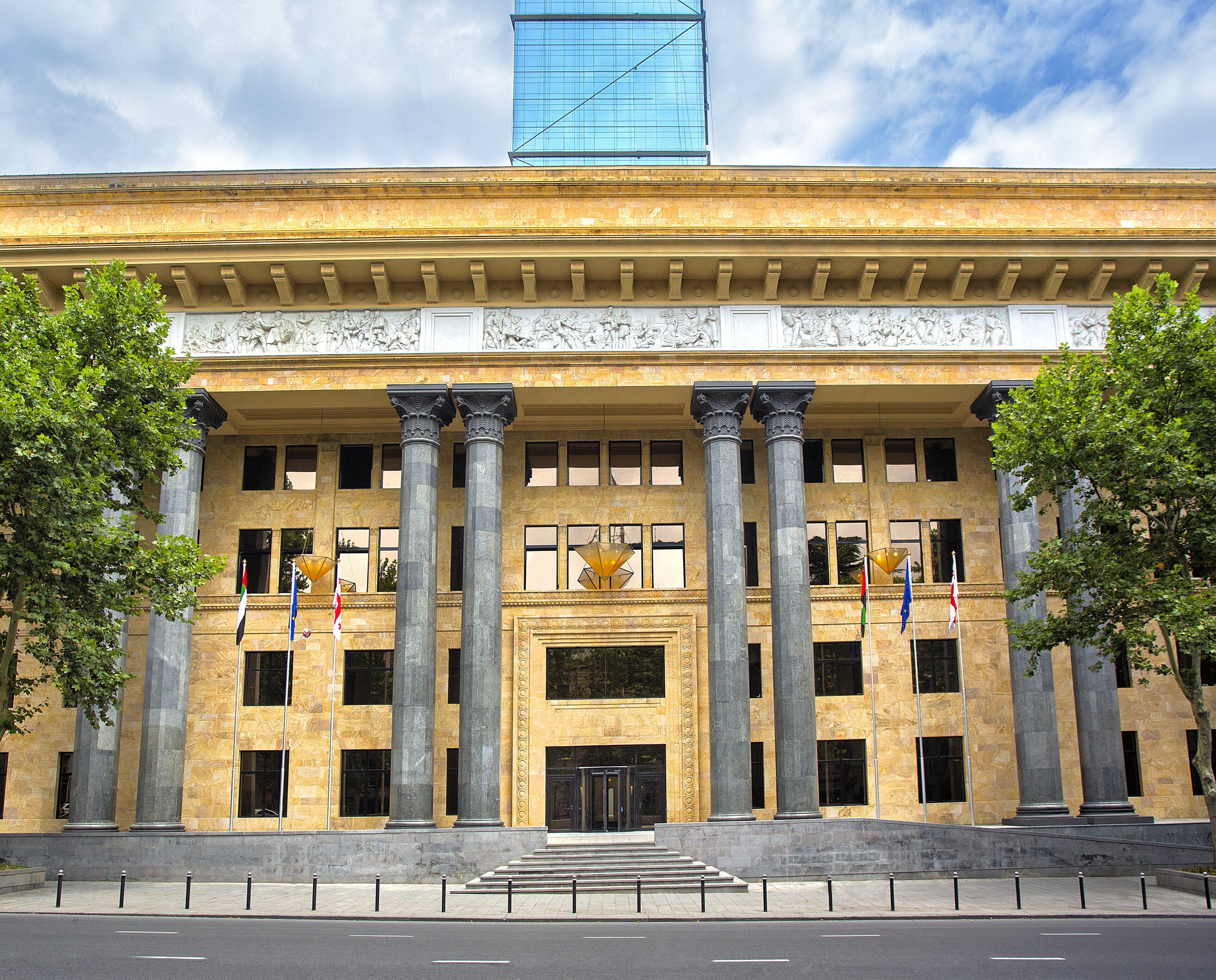 A large building with classical architecture, featuring tall columns, a central entrance, and multiple flags.