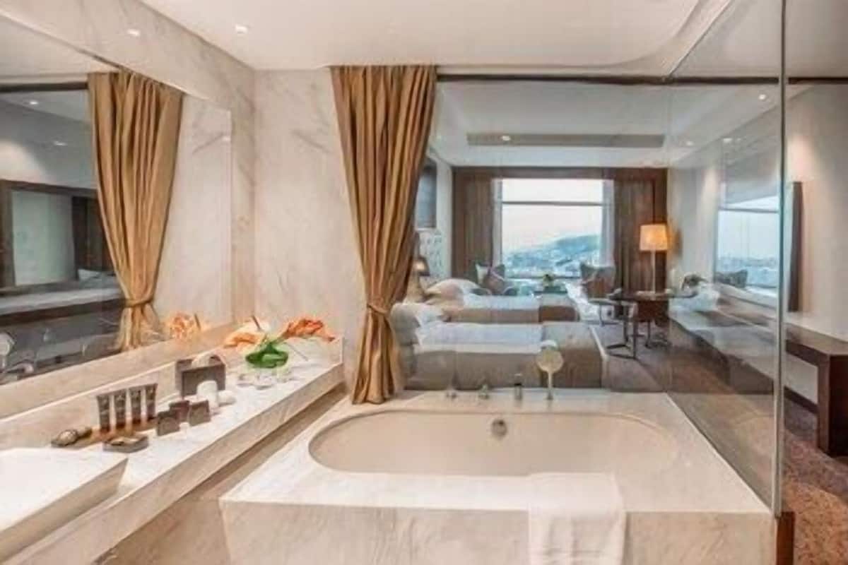 Ein modernes Badezimmer mit einer großen Badewanne, einem Waschtisch mit Spiegel und Blick auf ein Schlafzimmer mit Bett und Schreibtisch.