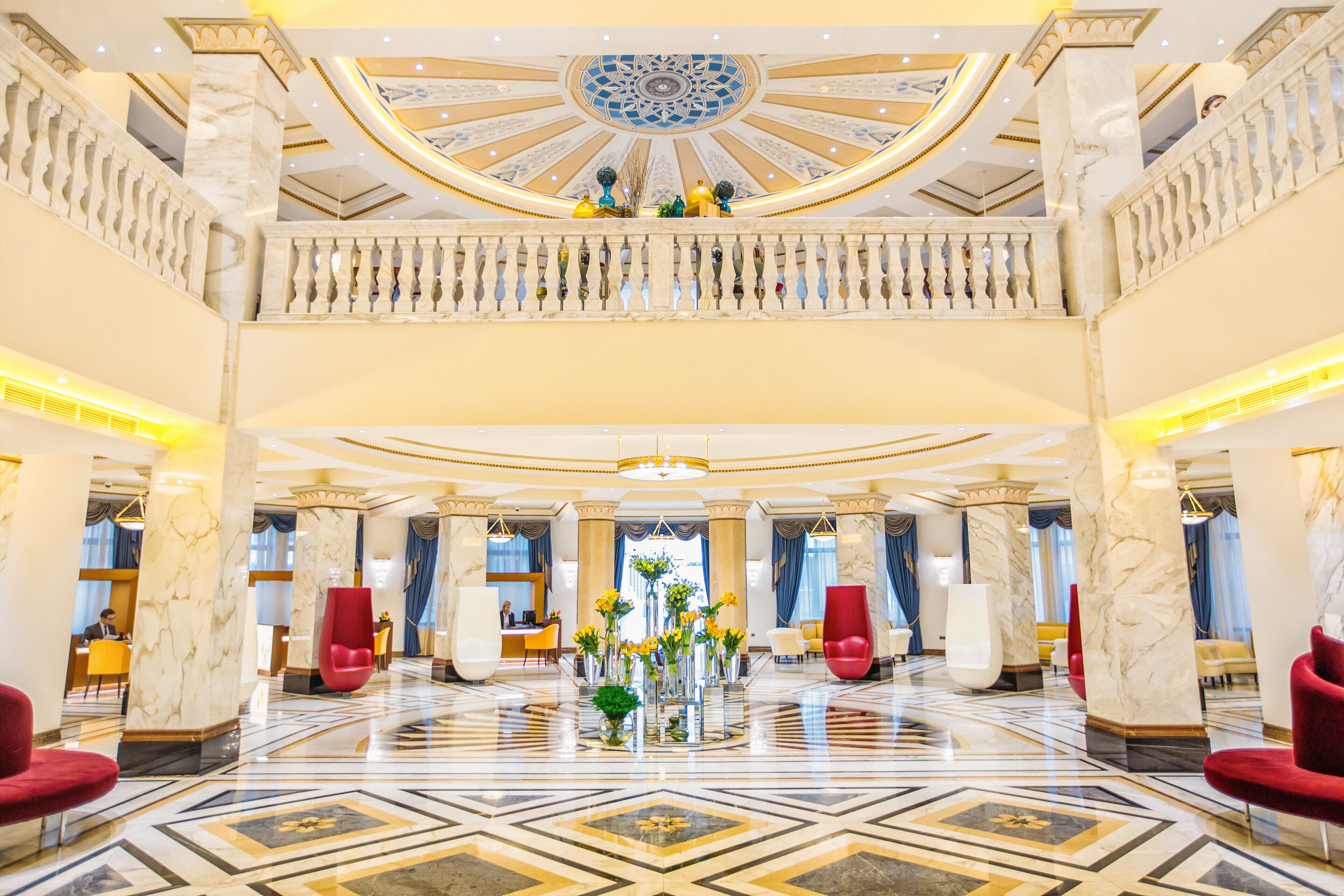 A grand lobby with marble floors, a central floral arrangement, and a high-ceiling with intricate designs.