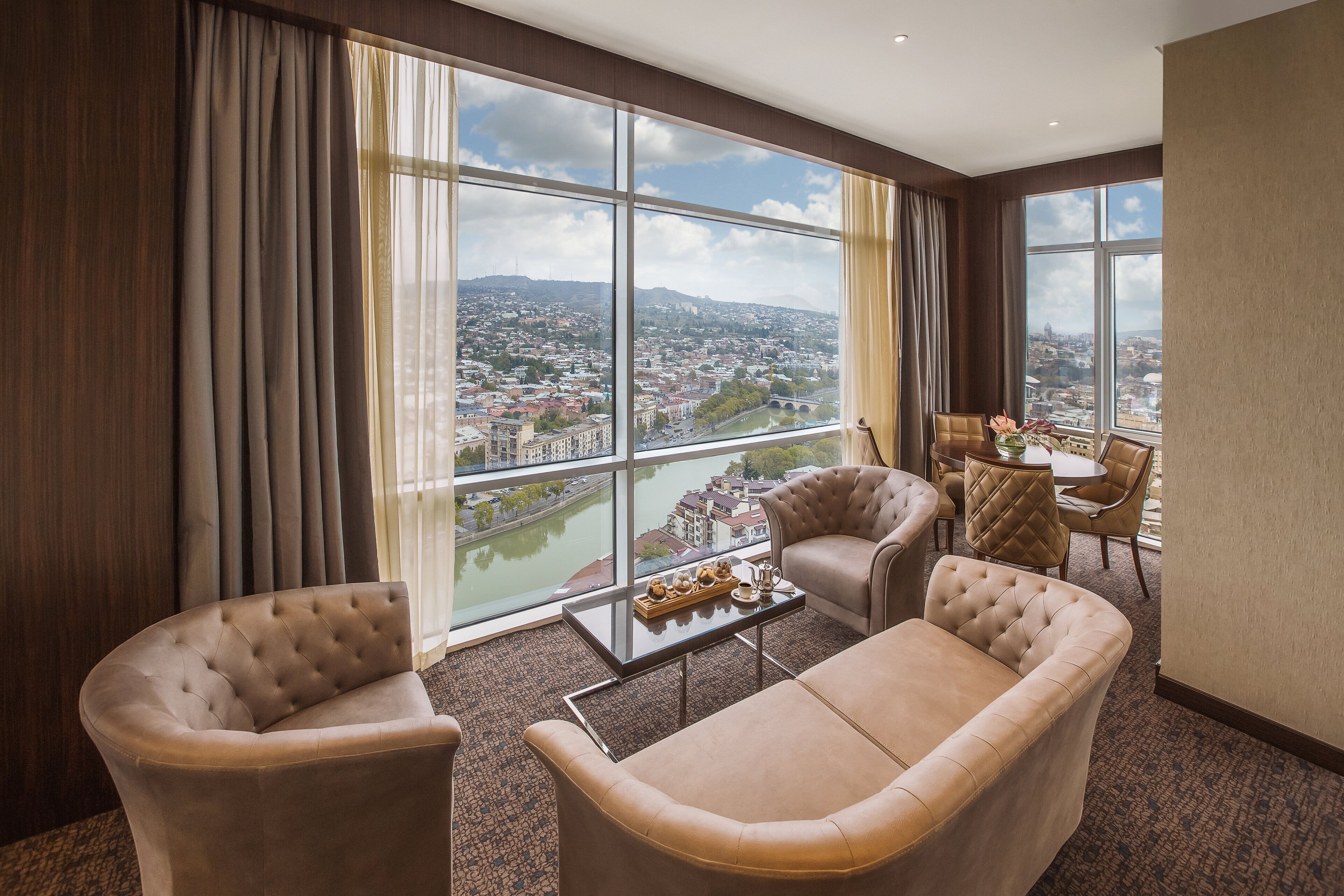 A spacious room with large windows offering a city view, a comfortable seating area, and a small table with decorative items.