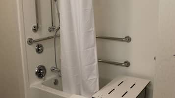 A bathroom with a bathtub, grab bars, a shower curtain, and a towel rack.