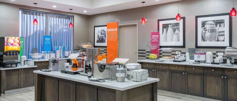 A modern hotel lobby with a reception desk, coffee machines, and framed pictures on the wall.
